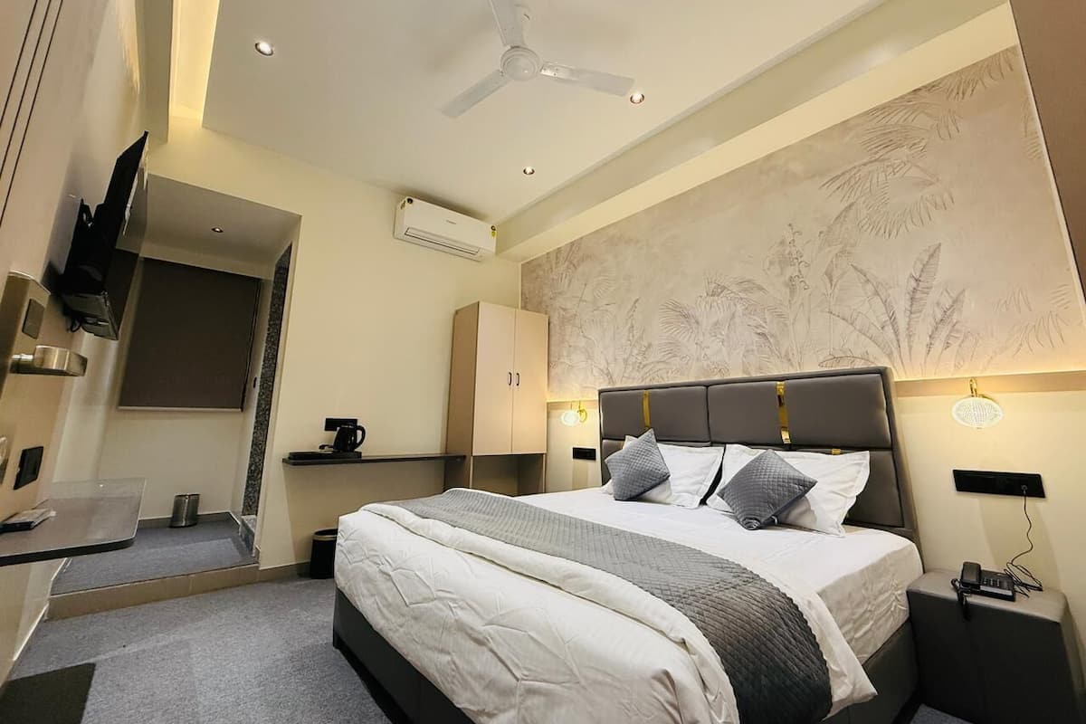 Habitación de hotel moderna con una cama grande, un escritorio, una silla, un ventilador de techo y un televisor montado en la pared.