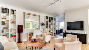 A modern living room with a large flat-screen TV, multiple seating areas, and extensive bookshelves. - Jardin des plantes - First concierge service (Montpellier)