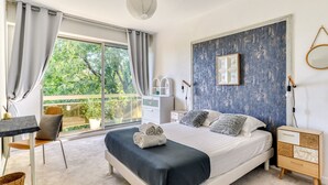 A bedroom with a large bed, a desk, a chair, and a view of greenery outside. - Jardin des plantes - First concierge service (Montpellier)