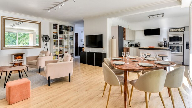 A modern living room with a dining area, a bookshelf, and a kitchen with a TV and a sign that reads "CHAMPAGNE". - Jardin des plantes - First concierge service (Montpellier)