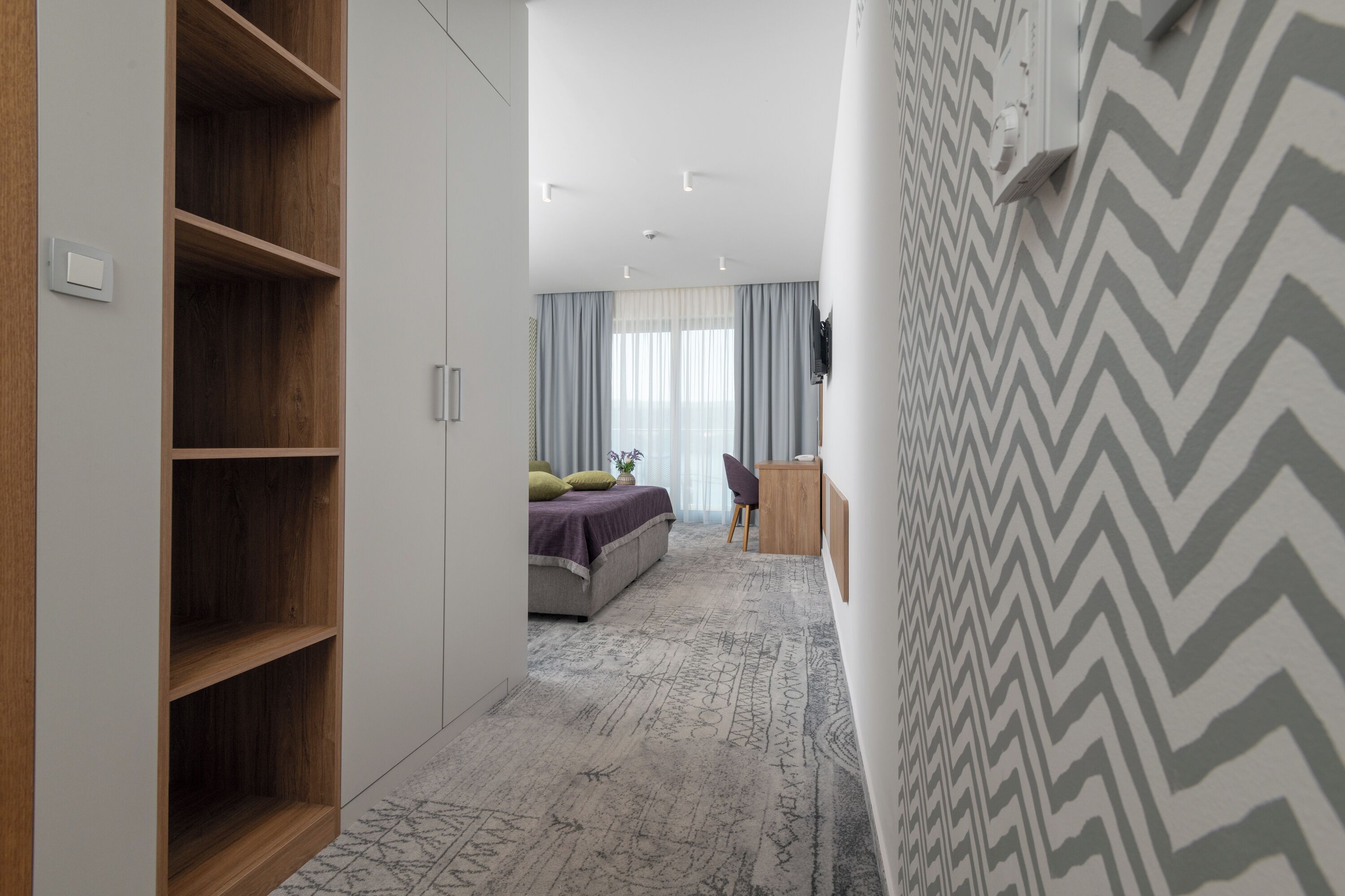 A modern bedroom with a large wardrobe, a bed with a gray and white patterned rug, and a chevron-patterned wall.