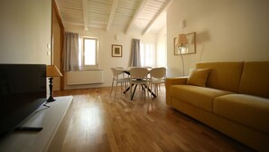 Een woonkamer met houten vloer, een gele bank, een eettafel met stoelen, een televisie en een lamp.