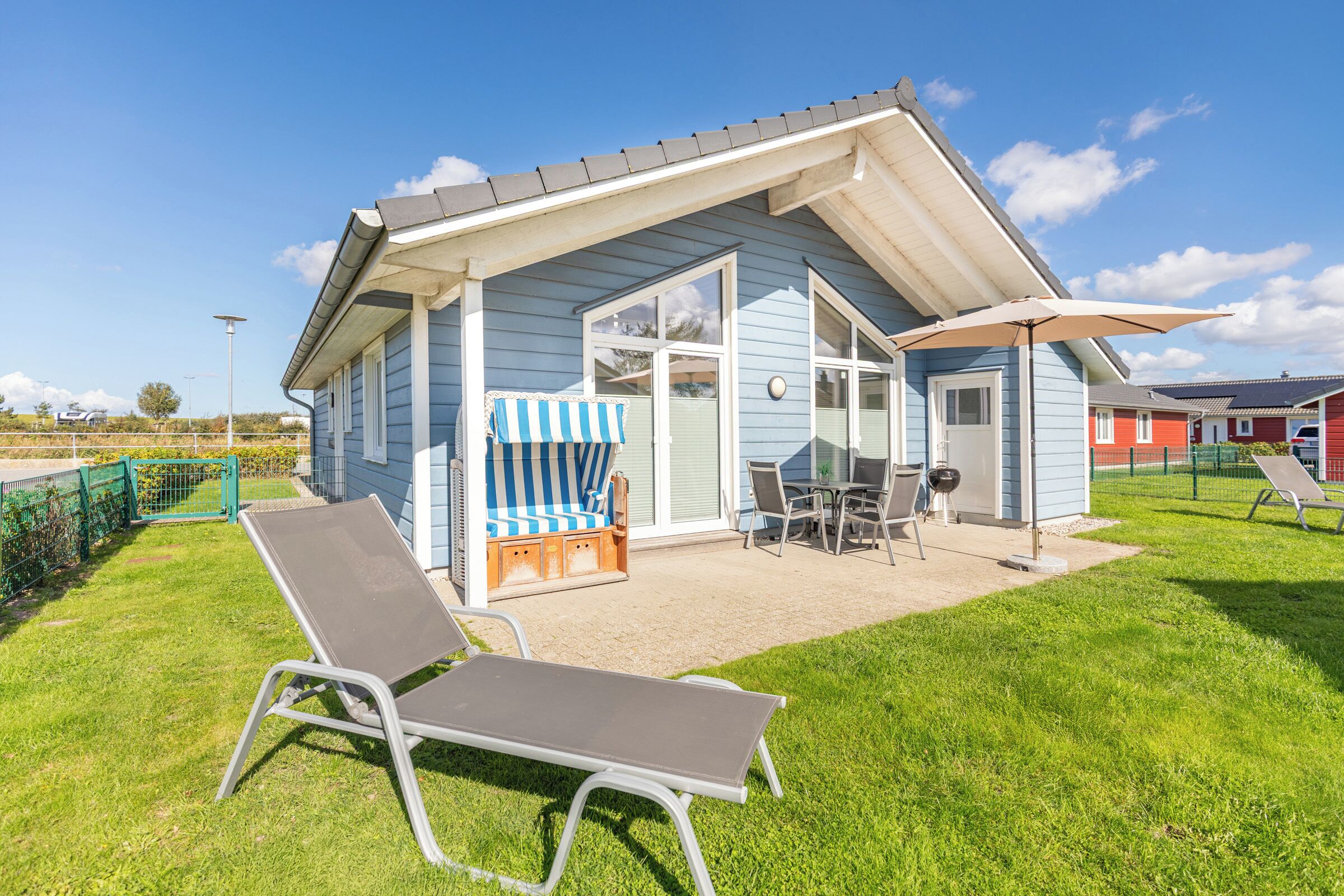 A blue house with a patio, a striped chair, a table, and a sun lounger.