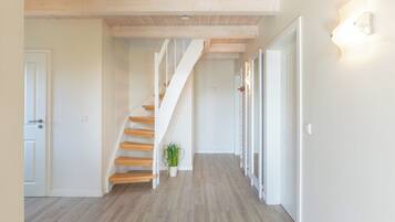A hallway with a wooden staircase, white walls, and a potted plant.
