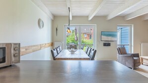 A modern kitchen with a large island, dining table, and chairs. There is a clock on the wall, a window with a view of the outdoors, and a television mounted on the wall. - Vacation home "Fischerhuus" in Dagebüll for up to 7 people (Dagebüll)