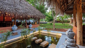 Un espace extérieur paisible, doté d’une structure à toit de chaume, d’un bassin d’eau décoratif et de bancs en pierre.