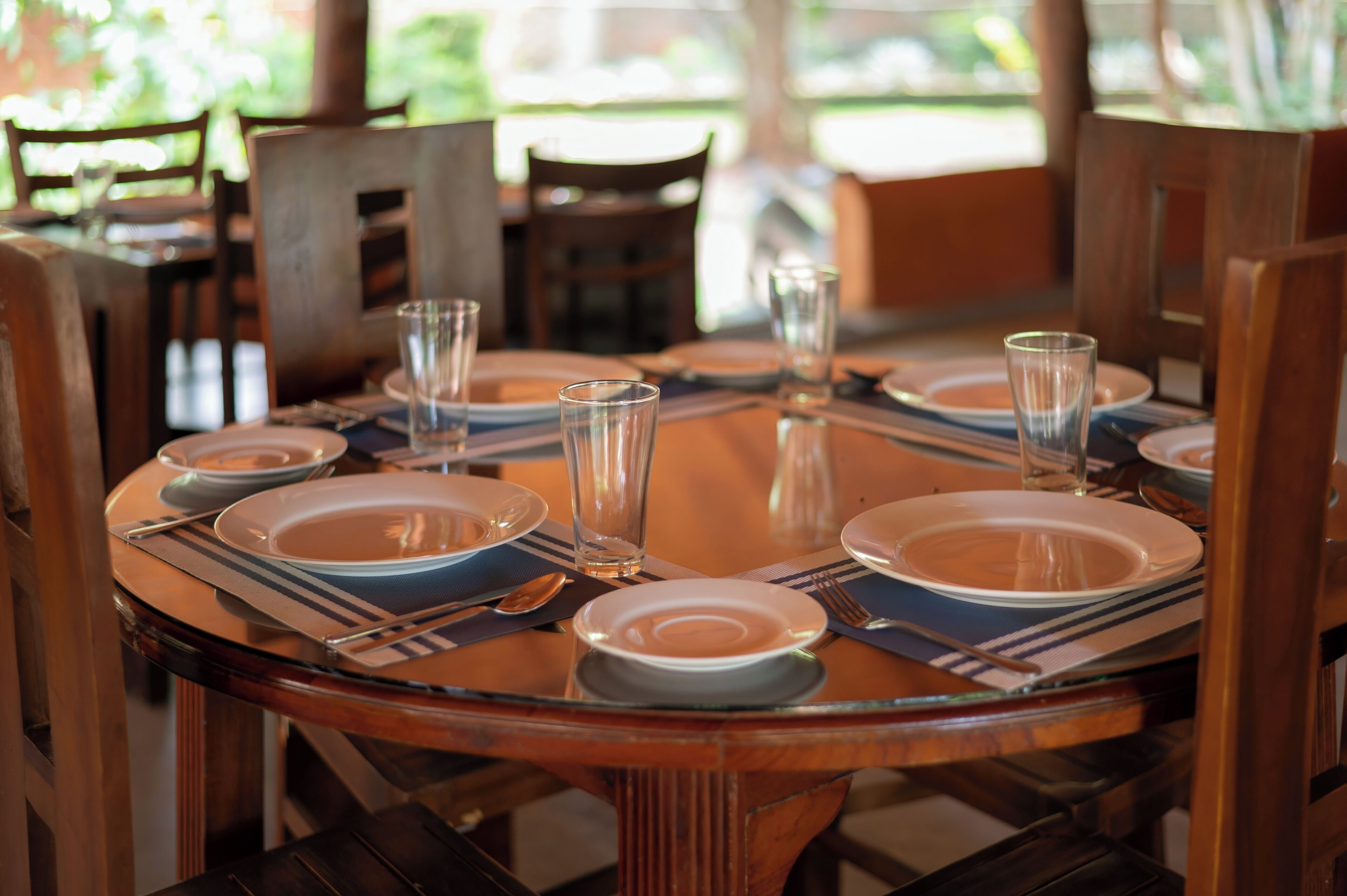 A round dining table set for four with clear glassware and plates, surrounded by wooden chairs.