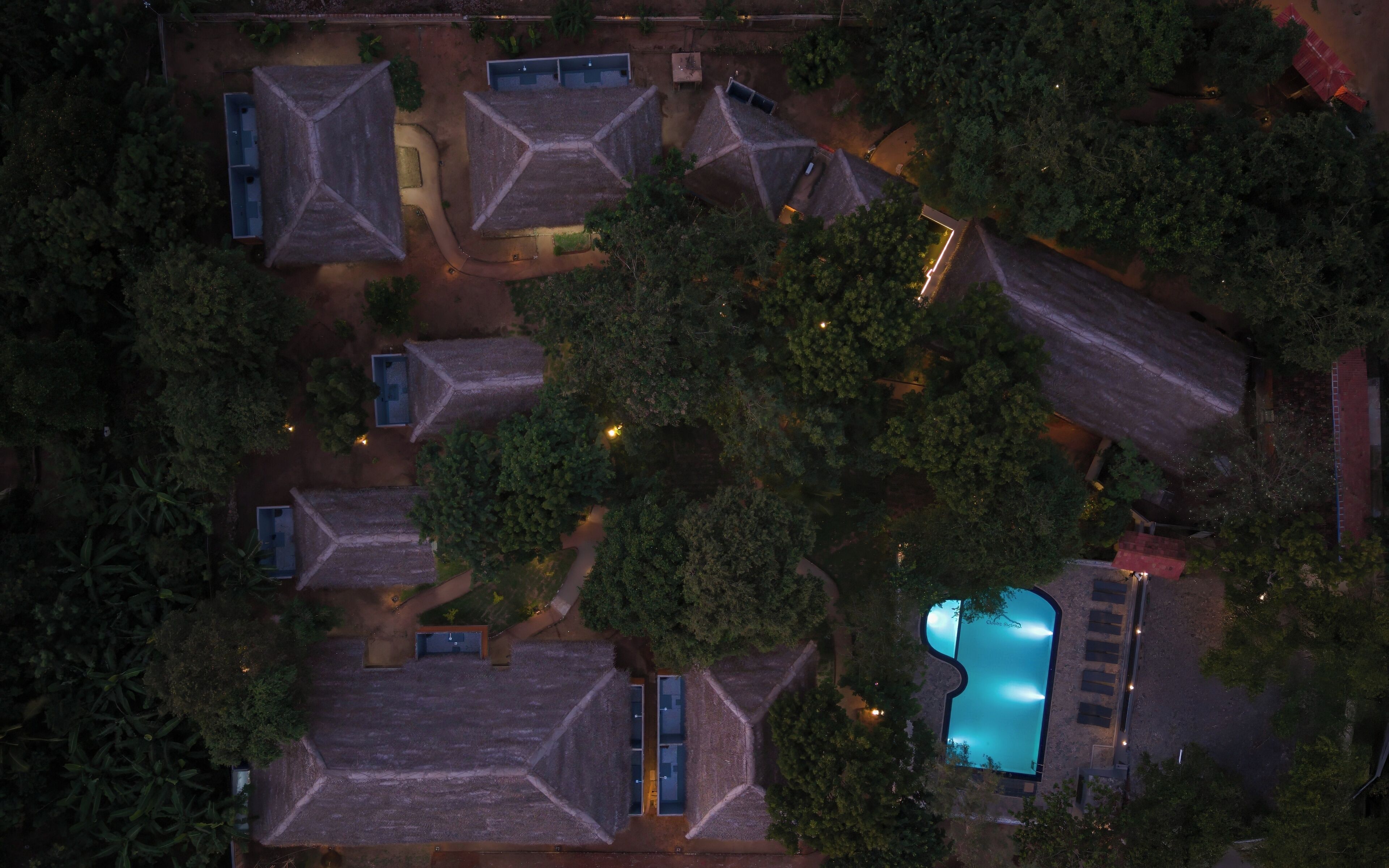 Vista aérea de un resort con varias cabañas de techo de paja, una piscina y abundante vegetación circundante.
