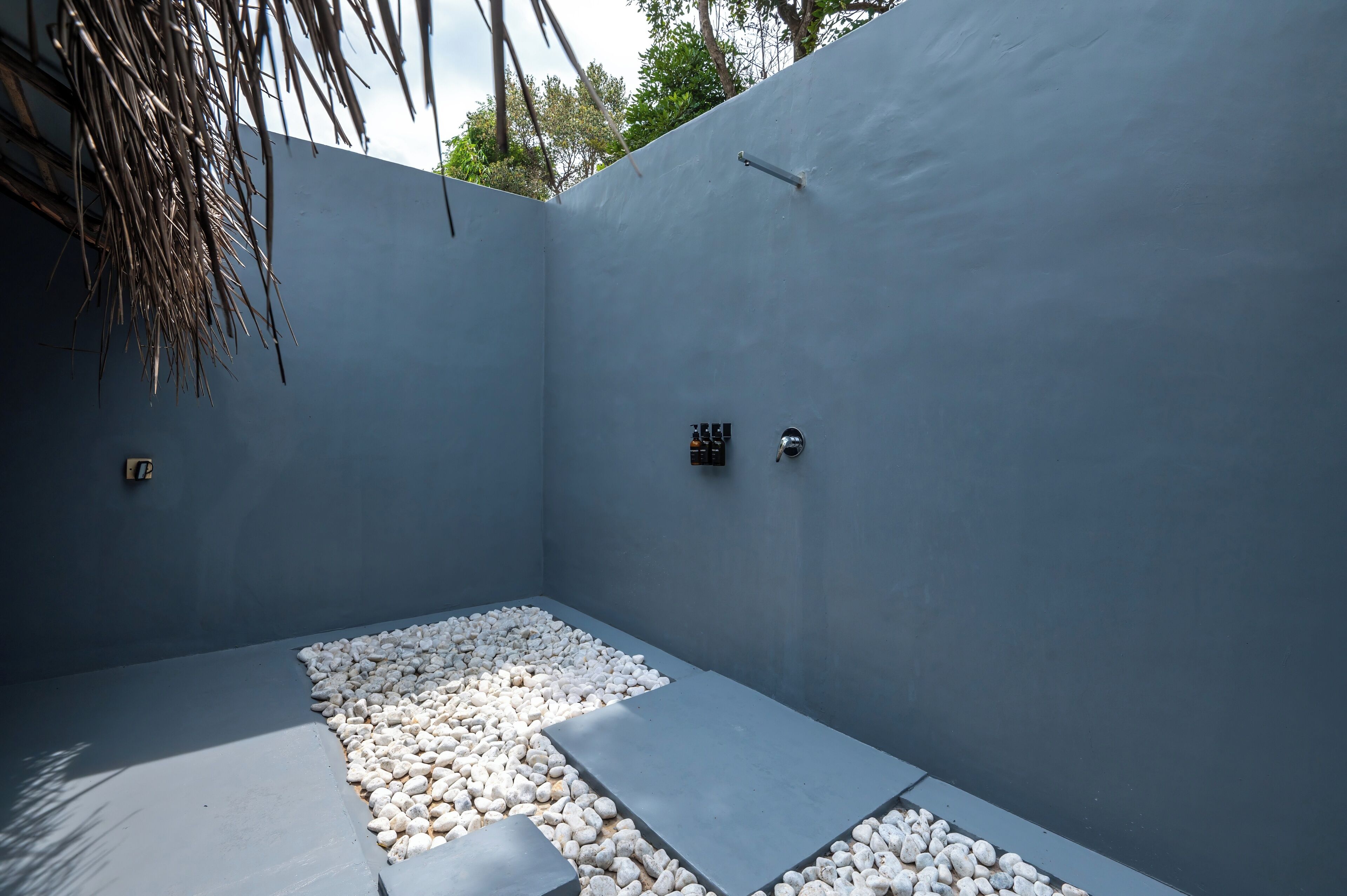 A modern, minimalist outdoor space with a concrete floor, white pebbles, and a blue wall.