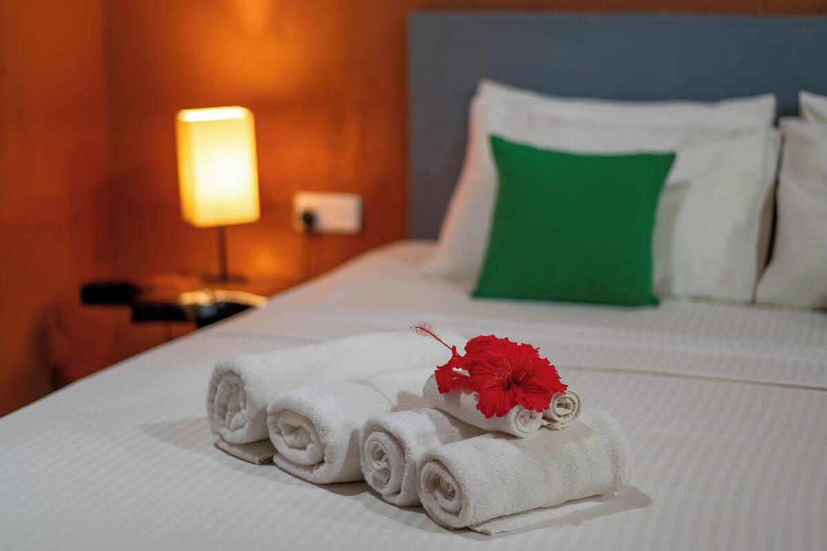 Una cama bien tendida con sábanas blancas, un almohadón verde y una decoración floral roja.
