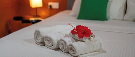 A neatly made bed with white linens, a green pillow, and a red flower decoration.