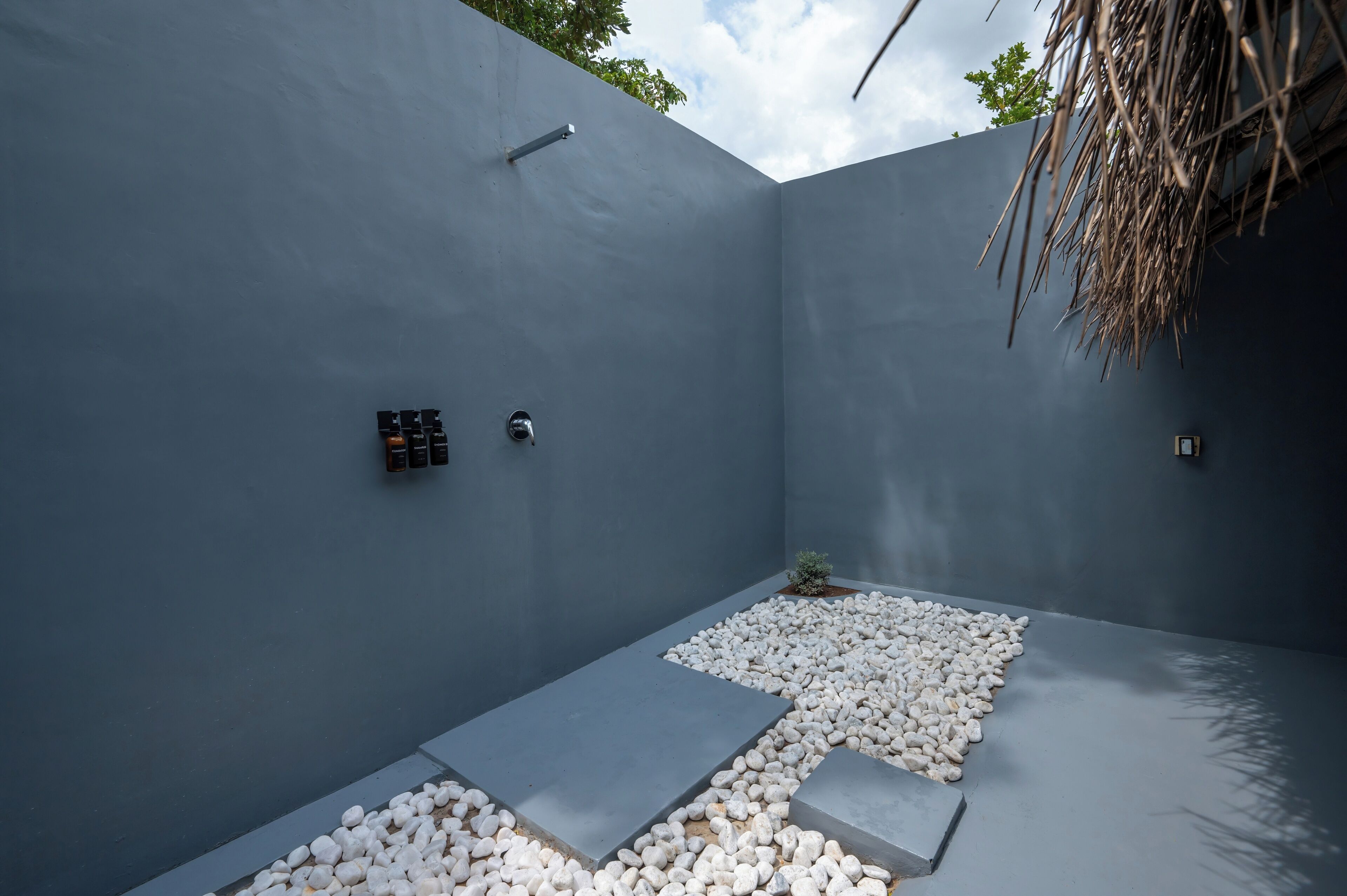 A modern outdoor space with a grey wall, a small garden area with white pebbles, and a thatched roof structure.
