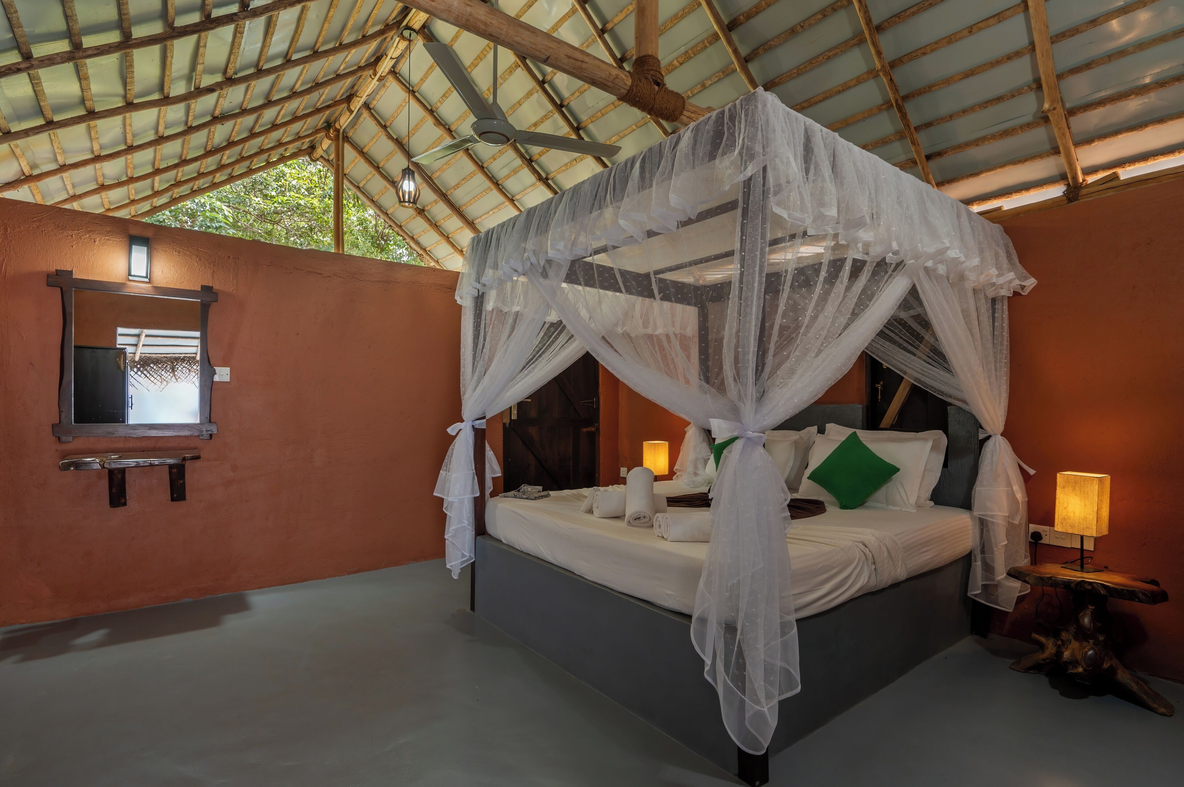 A room with a bed under a canopy, a bedside table with a lamp, a wall-mounted TV, and a ceiling fan.