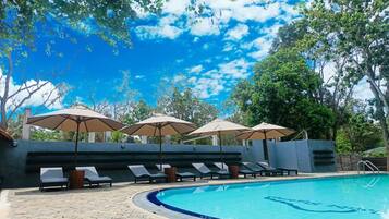 A swimming pool with lounge chairs and umbrellas, surrounded by trees and a clear sky.