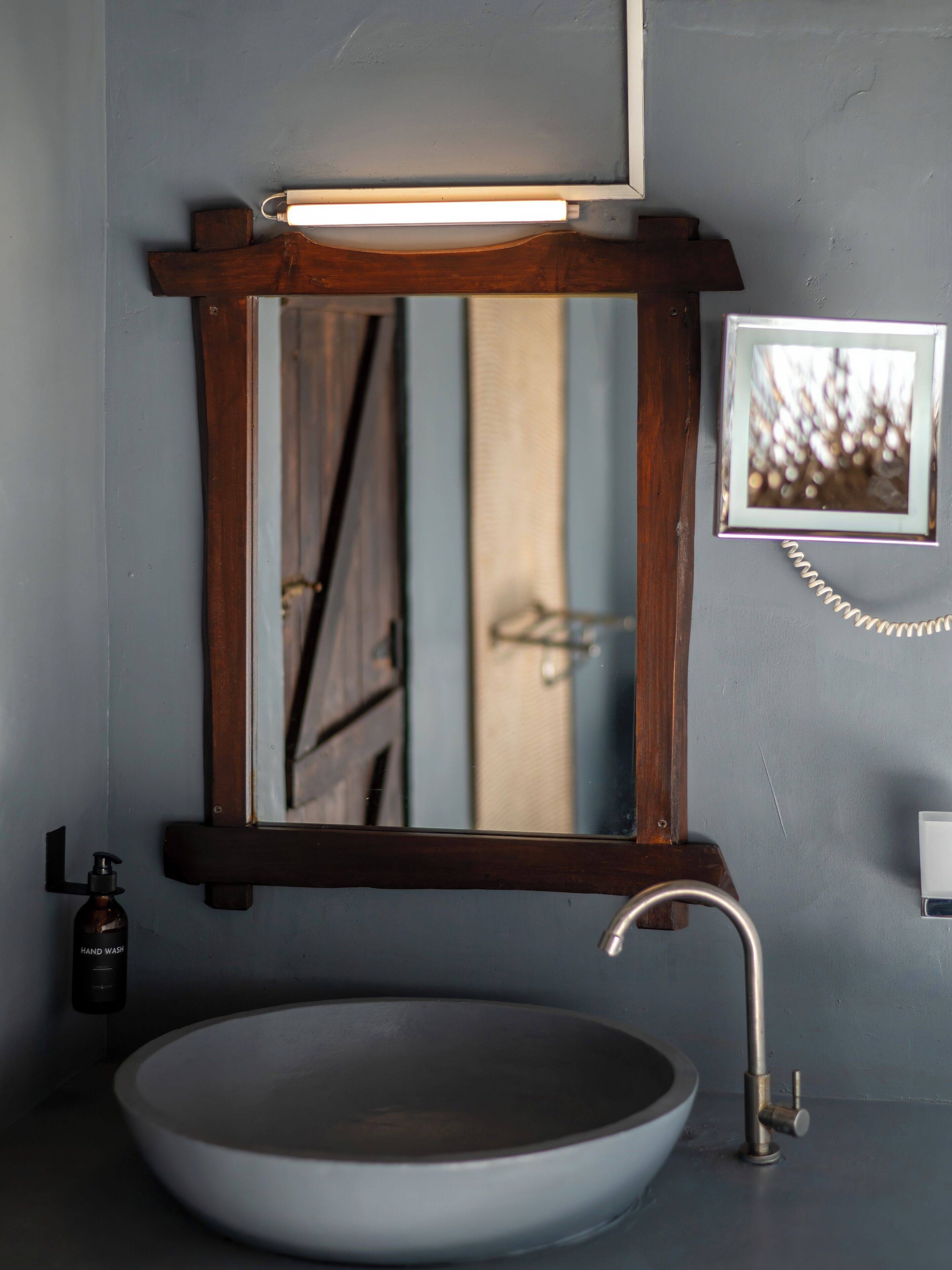 Une salle de bain avec un lavabo rond, un miroir encadré en bois, un distributeur de savon liquide et une photo encadrée accrochée au mur.