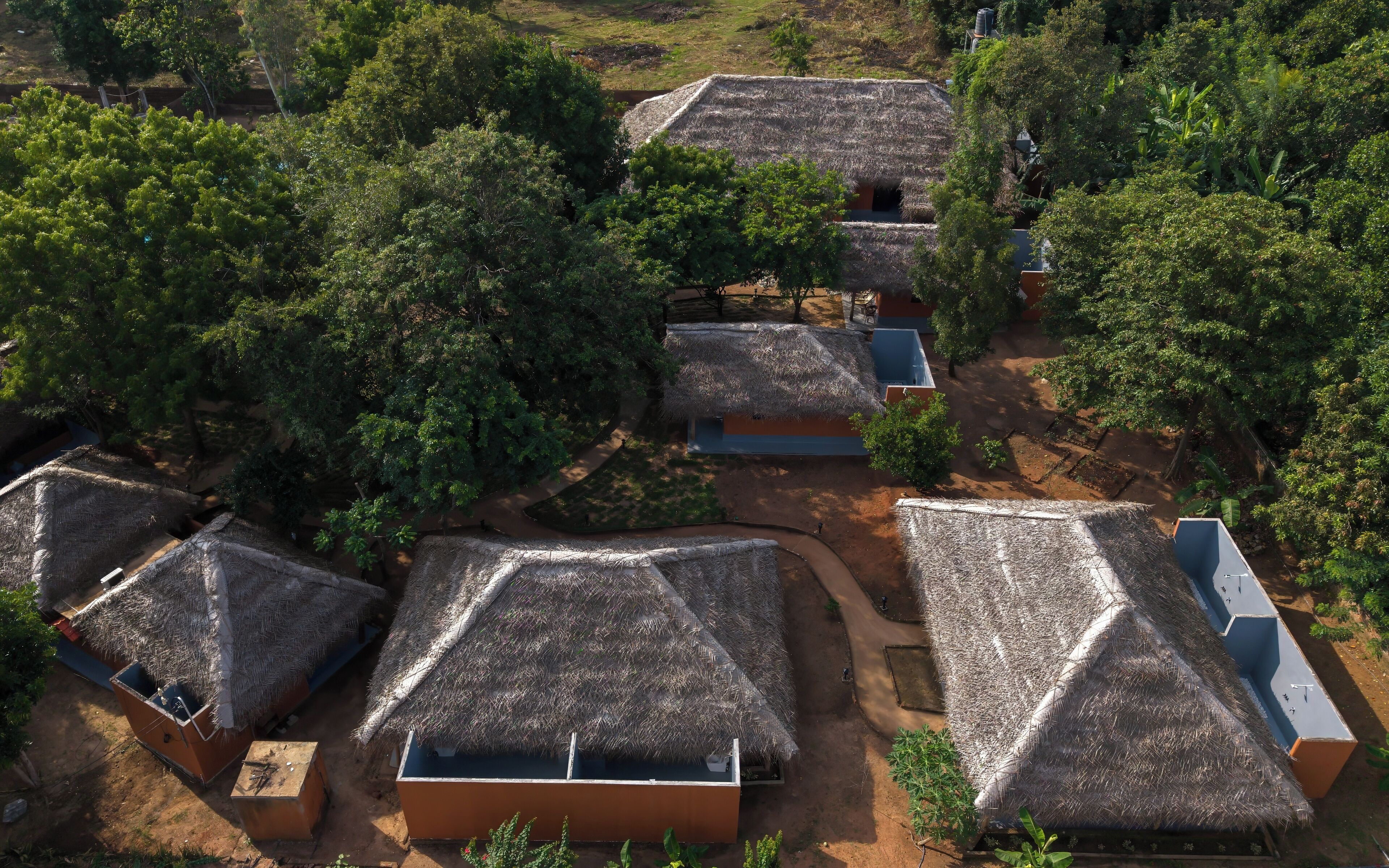 A cluster of thatched-roof huts with rectangular structures, surrounded by dense greenery.