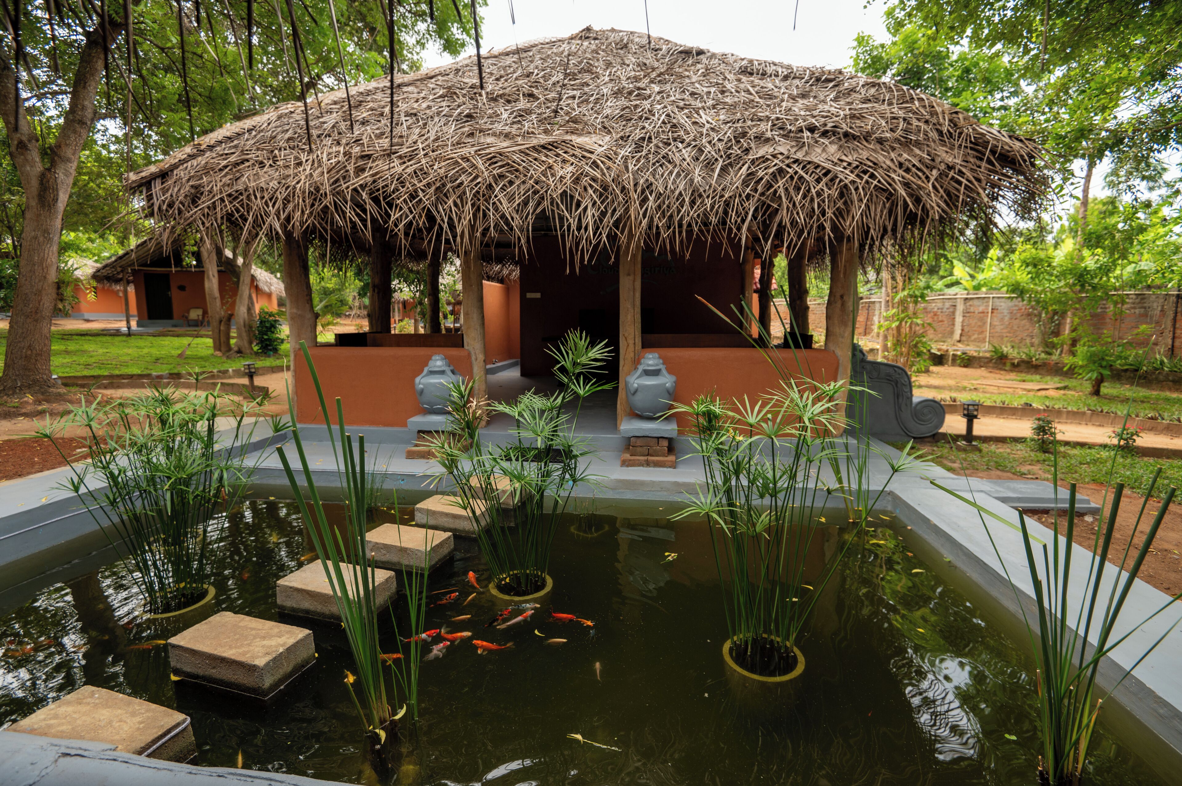 A thatched-roof pavilion with a koi pond in front.
