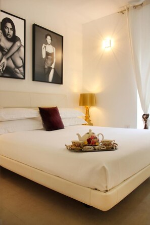 A hotel room with a bed, a bedside table with a lamp, a tray with tea set, and two framed pictures on the wall. - Reggia del Saraceno – Luxury House in the Heart of Ortigia (Siracusa)