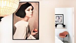 A framed portrait of a person holding an apple, a modern chair, and a bed with a white headboard. - Reggia del Saraceno – Luxury House in the Heart of Ortigia (Siracusa)
