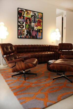 A sectional sofa with a swivel base, a patterned rug, and a wall art piece. - Reggia del Saraceno – Luxury House in the Heart of Ortigia (Siracusa)
