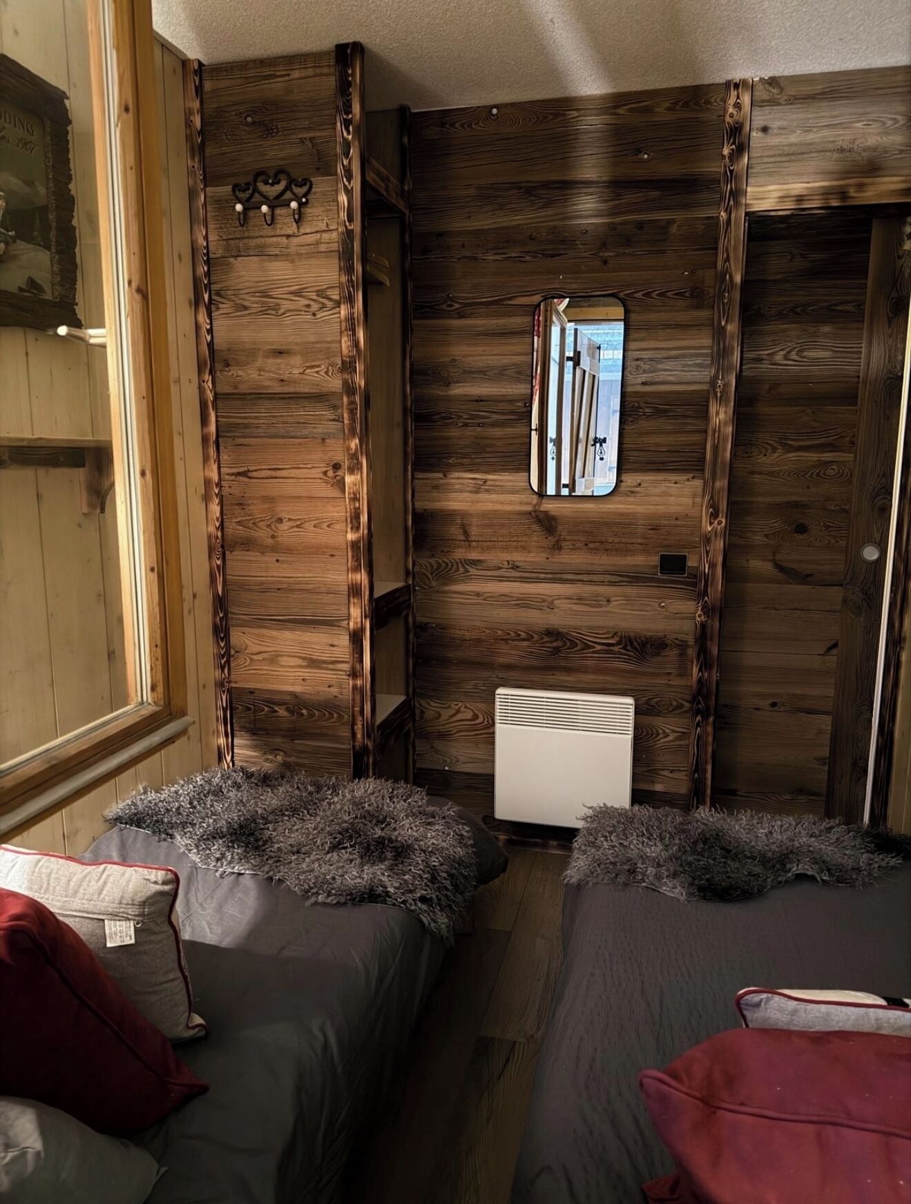 A compact room with two beds, a mirror, and a radiator.