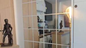 Huone, jossa on väliseinä, ruokailutila, jossa on tuoli, pieni pöytä, jossa on esineitä, ja keittiötila, joka on näkyvissä väliseinän läpi.