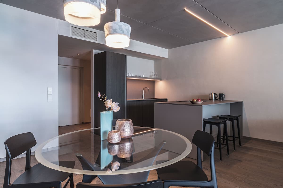 A modern kitchen with a round glass table, black chairs, and a small island with a sink and kettle.