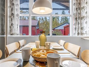 Un comedor con una mesa preparada para cuatro, un florero y una cesta de pasteles.