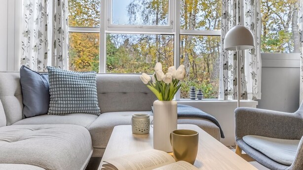 A modern living room with a sofa, armchair, and a coffee table. There is a book on the table, a vase with flowers, and a lamp. - "Catha" - 200m from the sea by Interhome (Væggerløse)