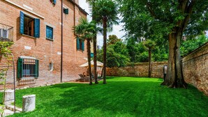 A courtyard with a brick building, green grass, palm trees, and a stone wall. - The Secret Garden of Venice Sanctuary: A Peaceful Getaway (Venezia)