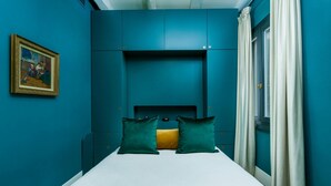 A bedroom with teal walls, a bed with white bedding, two teal pillows, and a framed picture on the wall. - The Secret Garden of Venice Sanctuary: A Peaceful Getaway (Venezia)