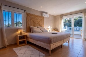 Ein Schlafzimmer mit einem großen Bett, einem Nachttisch, einem Fenster mit Gitter und Blick ins Freie.