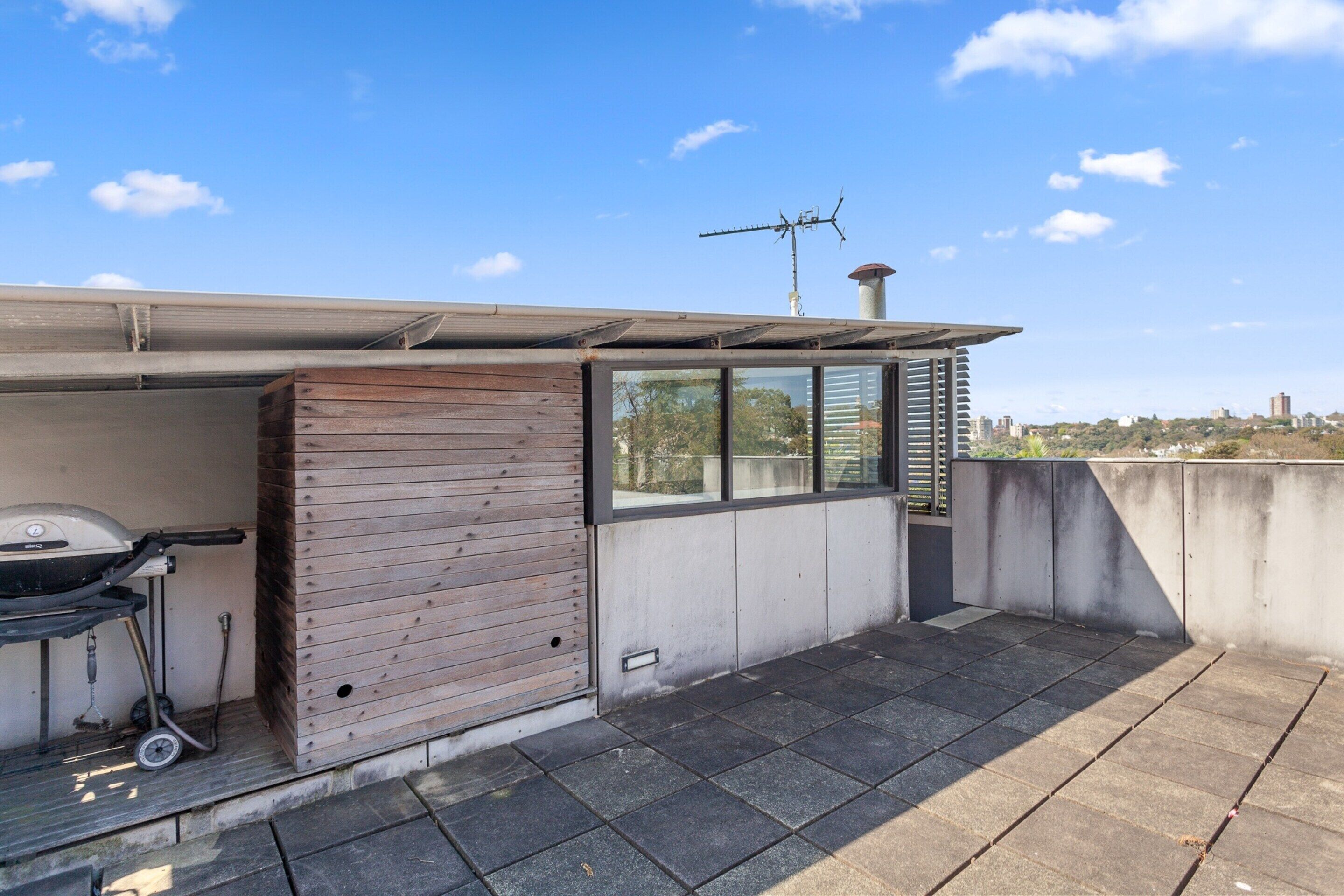 Eine Dachterrasse mit Grill, einer Holzverkleidung und Blick auf die Stadtlandschaft.