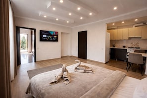 A modern hotel room with a large bed, a flat-screen TV, a kitchen area, and a balcony. - Villa Caza (Chișinău)