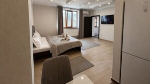 Una habitación de hotel moderna con cama, escritorio, silla, televisor de pantalla plana y refrigerador.