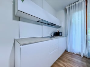 Eine moderne Küche mit weißen Schränken, einer Edelstahl-Arbeitsplatte, einer schwarzen Mikrowelle und einem Fenster mit weißen Vorhängen.