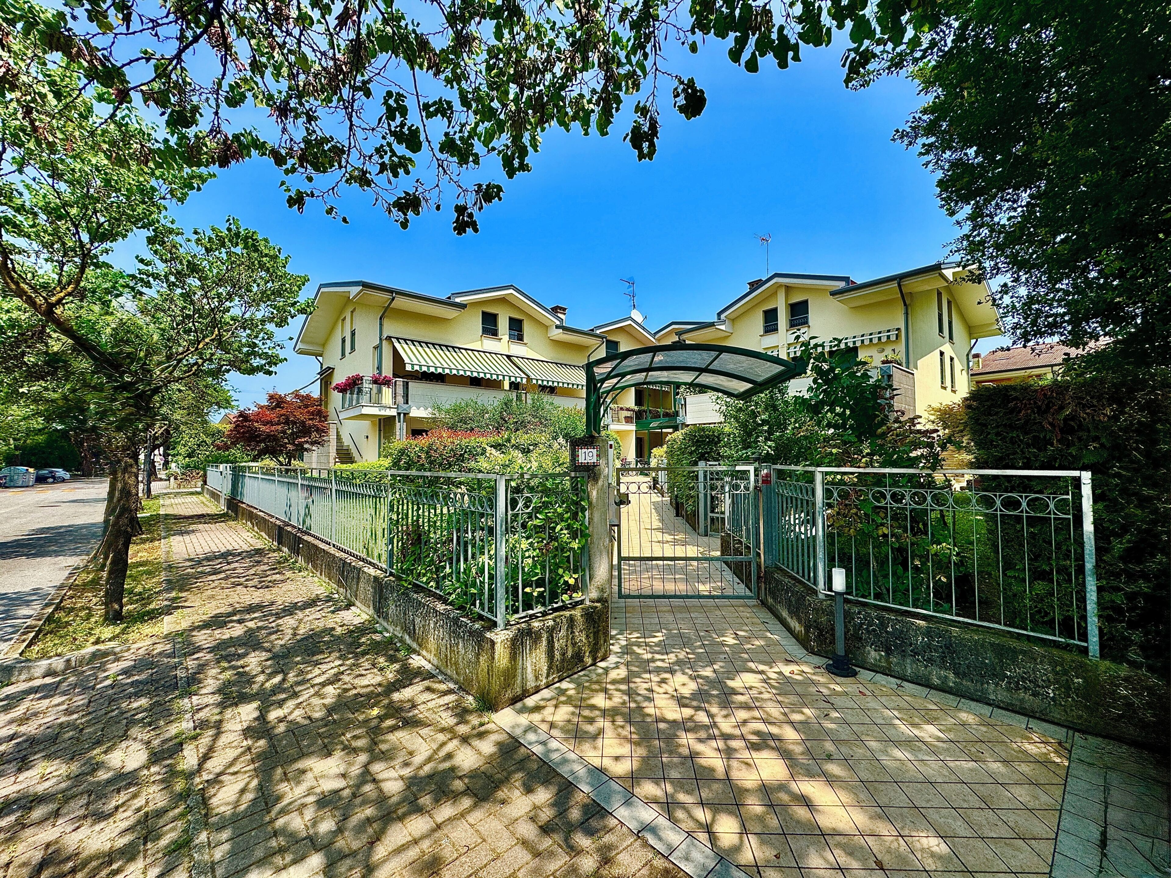 A residential building with a gated entrance, paved pathway, and surrounding greenery.