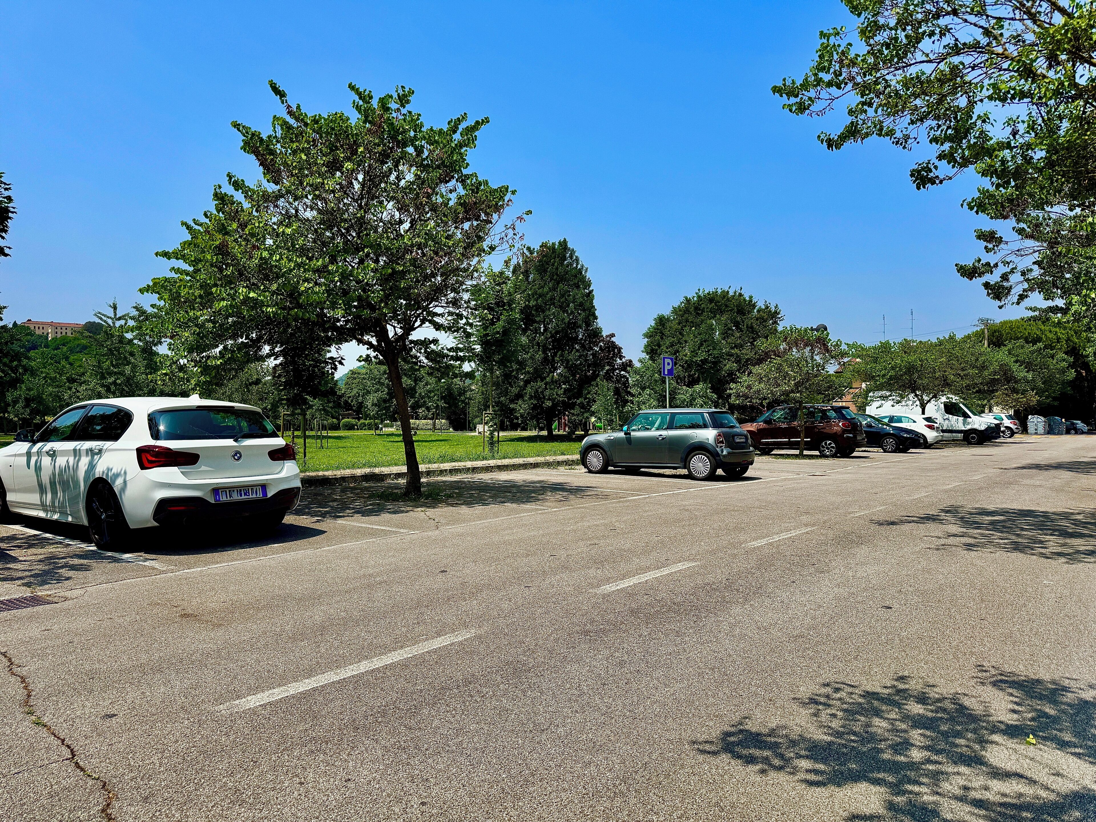 Un parcheggio con diverse auto, alberi e un cielo azzurro limpido.