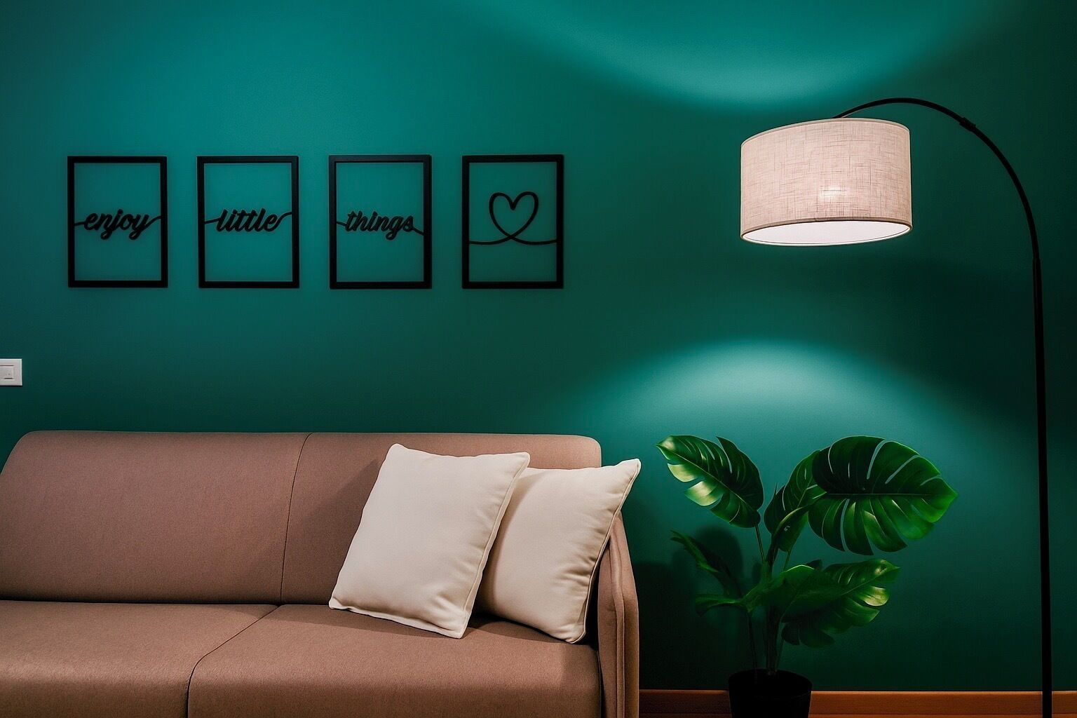 Een teal-kleurige muur met vier ingelijste borden met de tekst 'enjoy', 'little', 'things' en een hartsymbool. Daar tegenaan staat een bruine bank met twee kussens, en rechts ervan staat een vloerlamp.