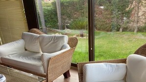 A room with wicker furniture, a glass table, and a view of a garden. - Frank's House, a villa surrounded by greenery with a private pool (Piana Calzata)