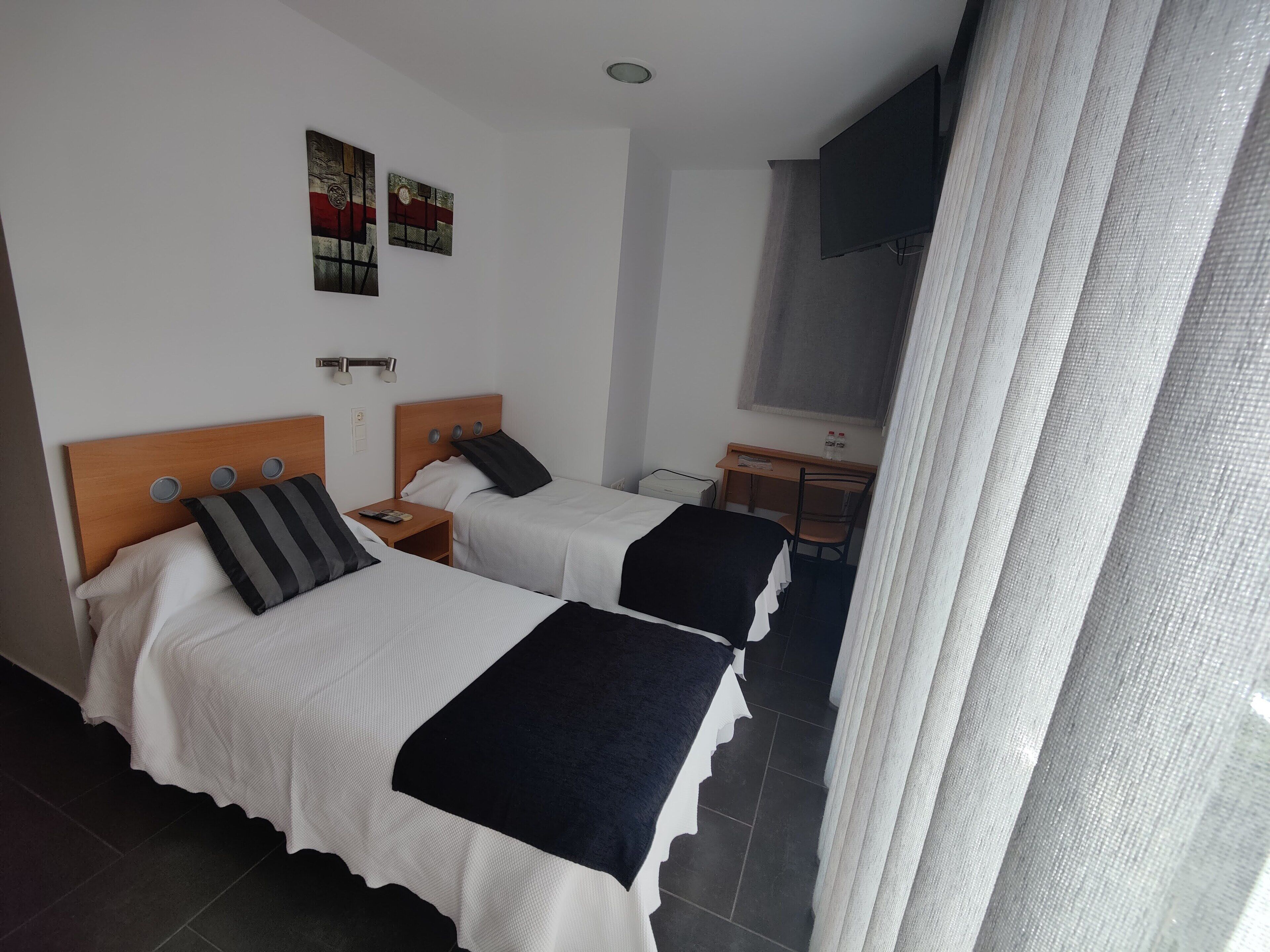A hotel room with two beds, a desk, a chair, and a TV.