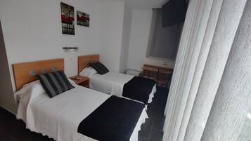 A hotel room with two beds, a desk, a chair, and a TV.