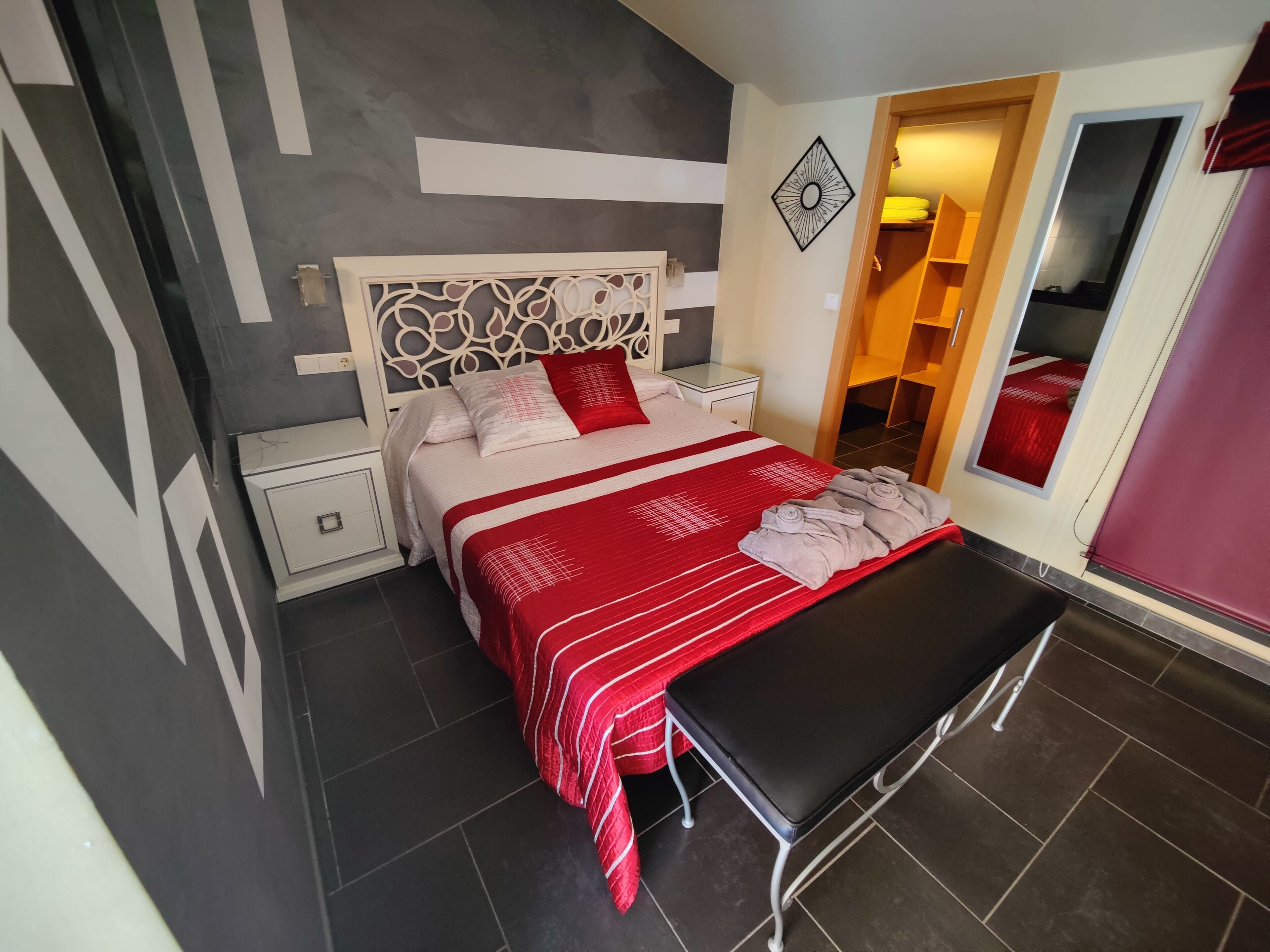 Un dormitorio moderno con cama, mesitas de noche, una banca y un espejo.