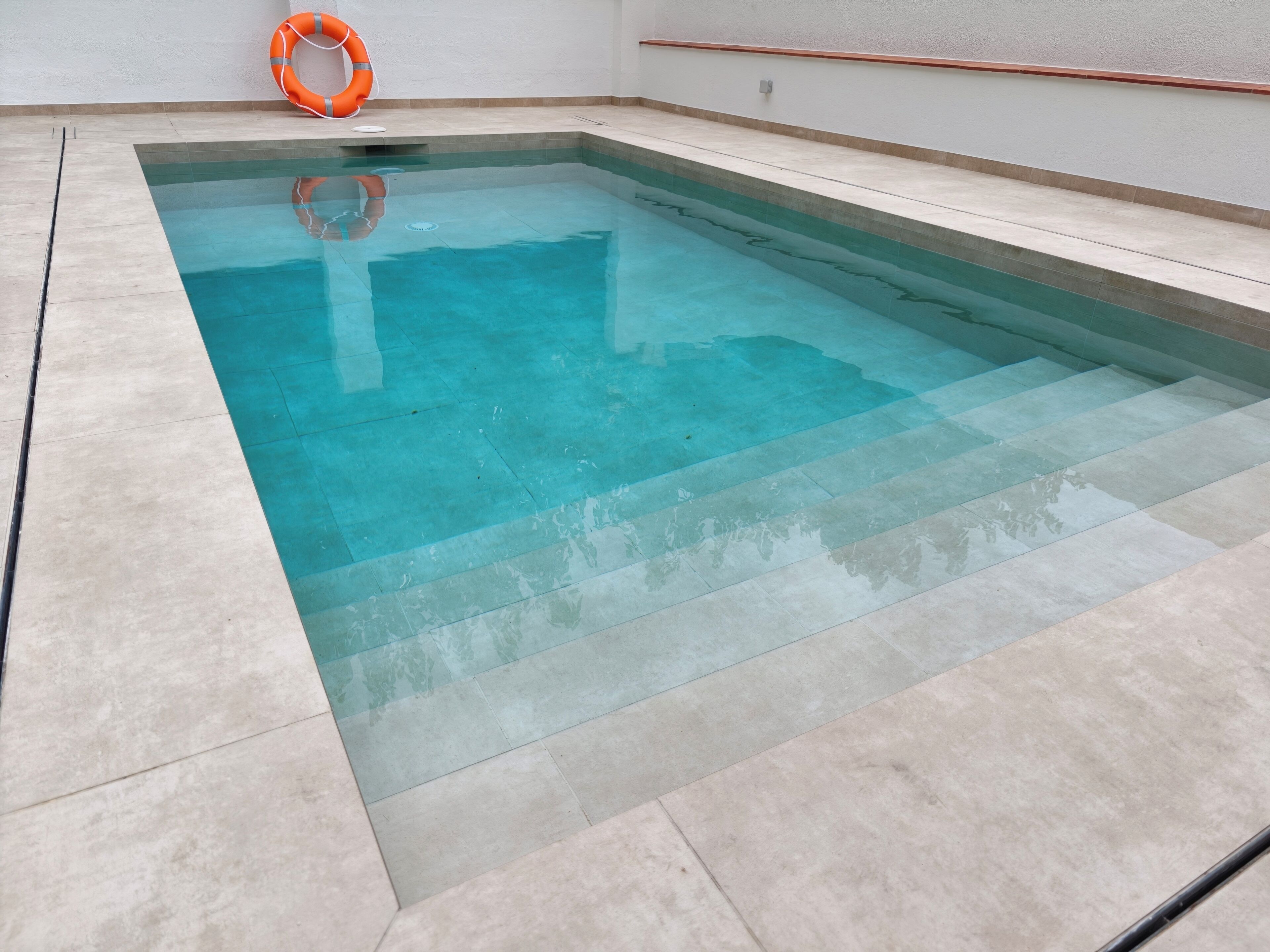 Una piscina rectangular con agua cristalina, rodeada por una solana con azulejos.