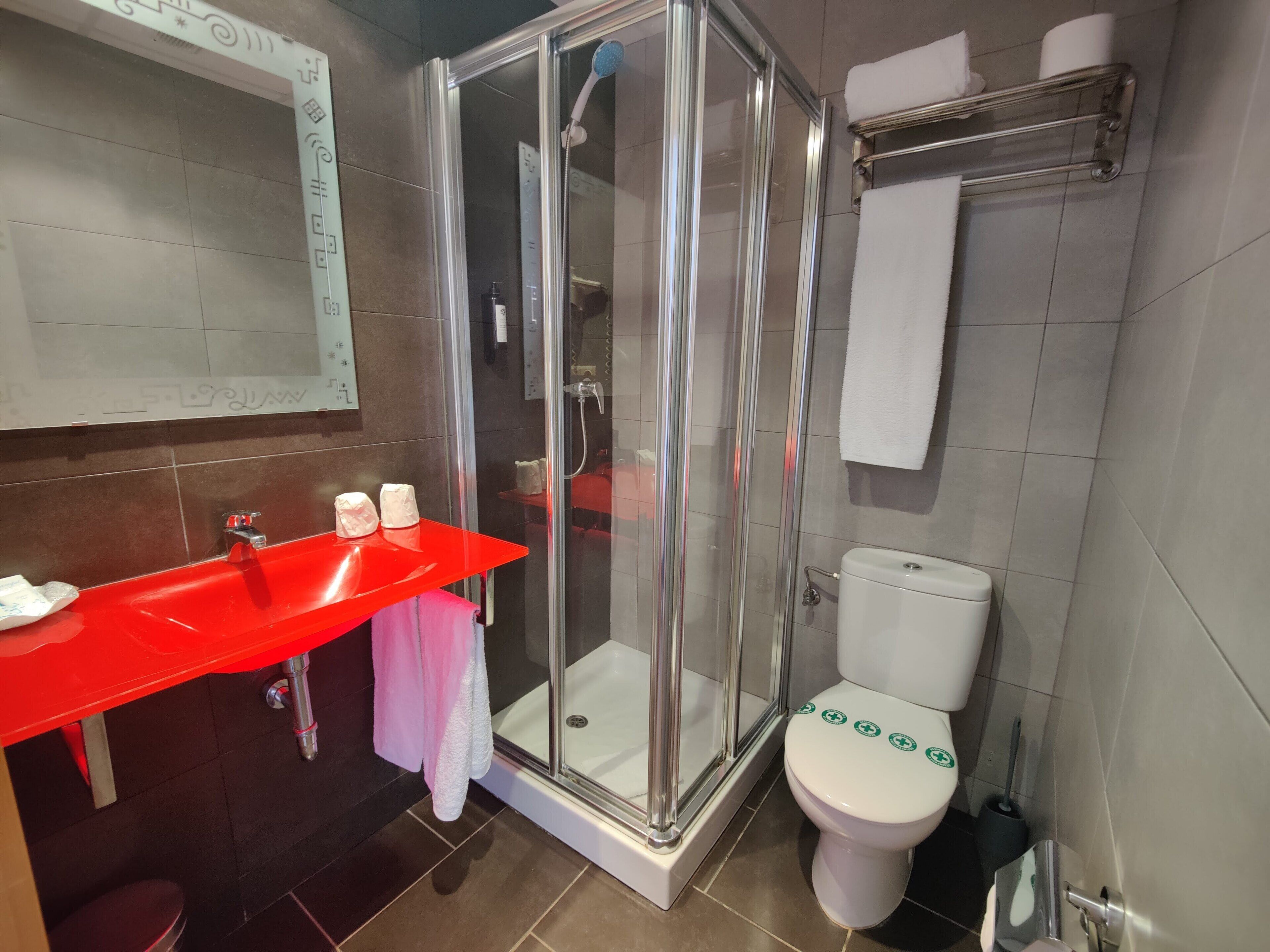 A modern bathroom with a glass-enclosed shower, a red sink, and a white toilet.