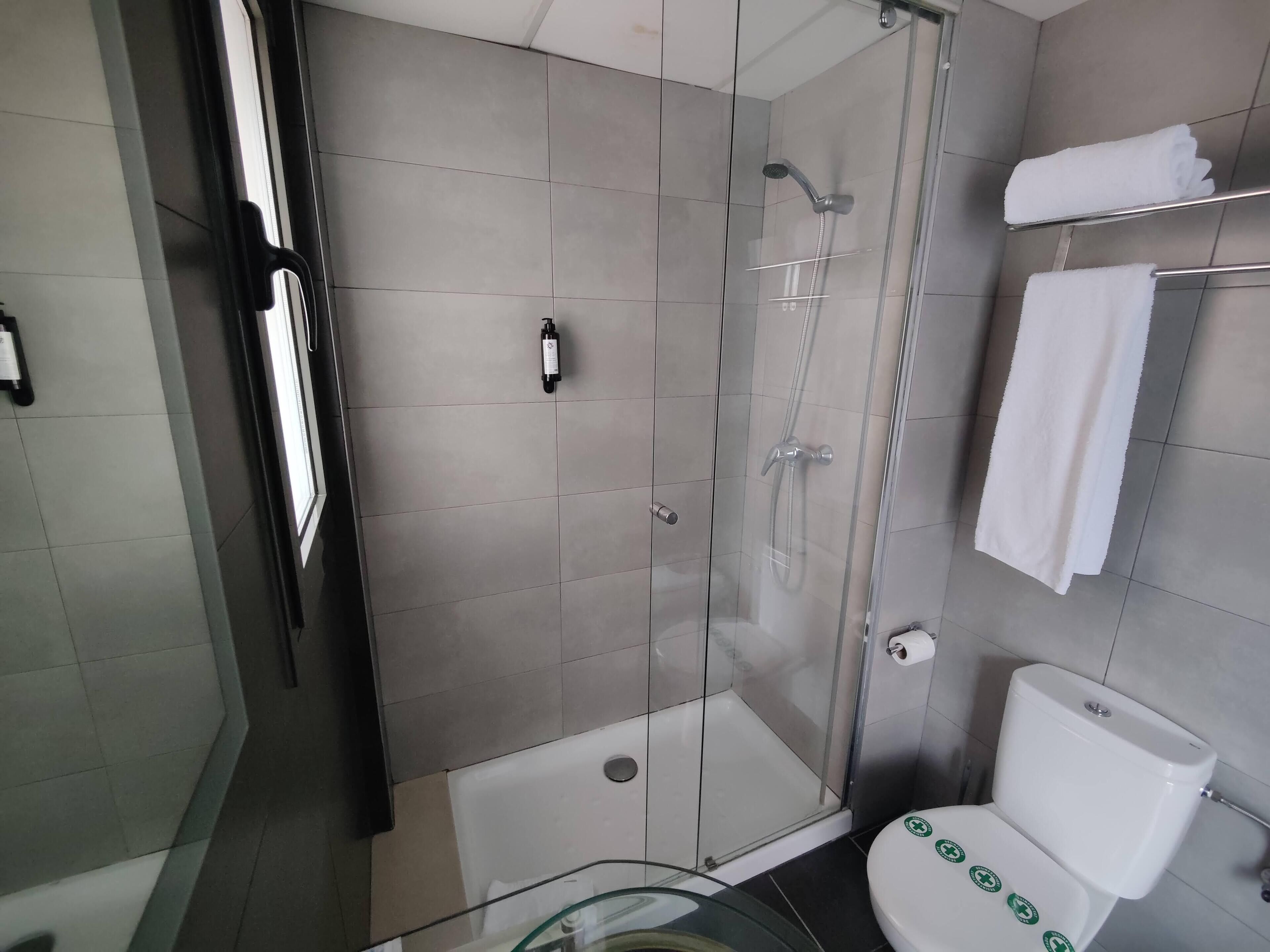 A modern bathroom with a glass-enclosed shower, a toilet with green stickers, and a towel rack with folded towels.