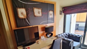 A compact room with a desk, a sofa, a TV, and an air conditioning unit. - Hostal Manel (Pineda de Mar)