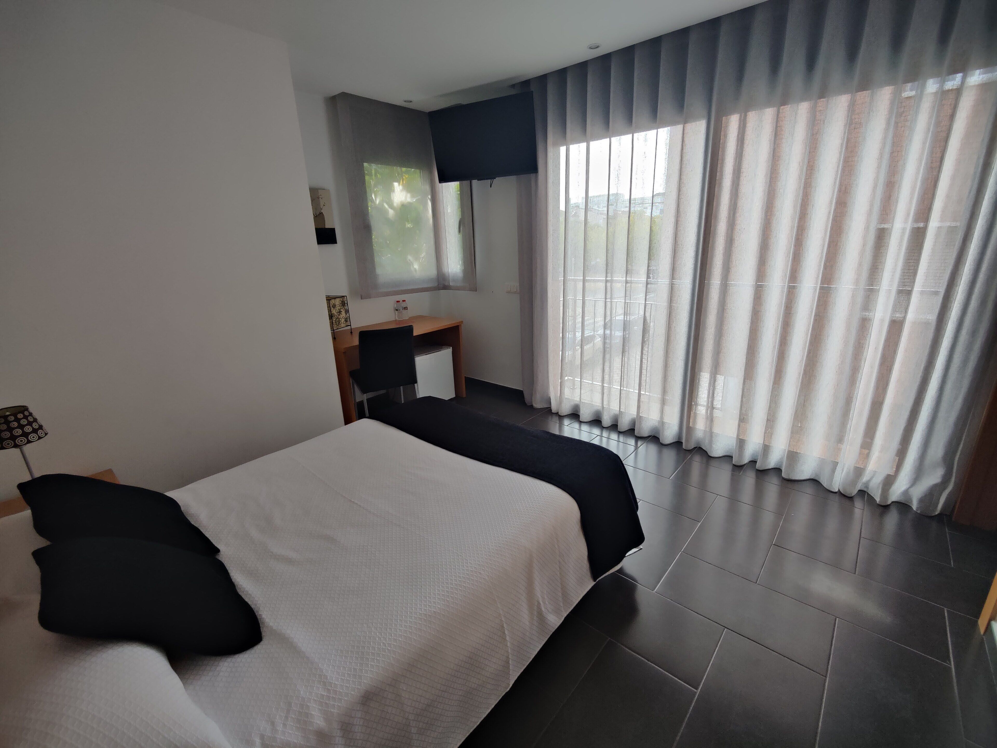 Habitación de hotel moderna con una cama grande, un escritorio y una silla. Tiene una ventana con cortinas y vistas al exterior.