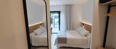 A hotel room with two beds, a mirror, a wooden headboard, a small table, and a view of the outside.