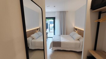 Habitación de hotel con dos camas, un espejo, cabecero de madera, una mesita y vistas al exterior.